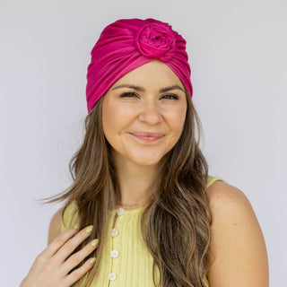 Woman wearing a bright pink turban with a flower design on a plain background