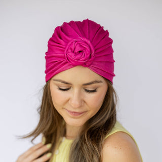 Woman wearing a bright pink headscarf with a flower design on a plain background