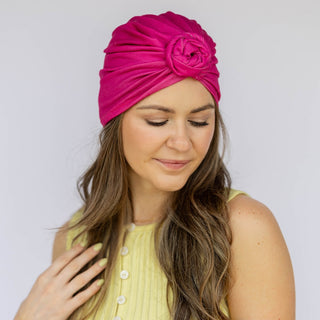 Woman wearing a bright pink headscarf with a flower design on a plain background